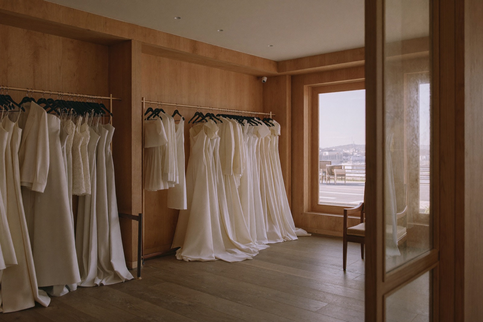 Inside a sunlit bridal boutique, racks of ivory gowns
